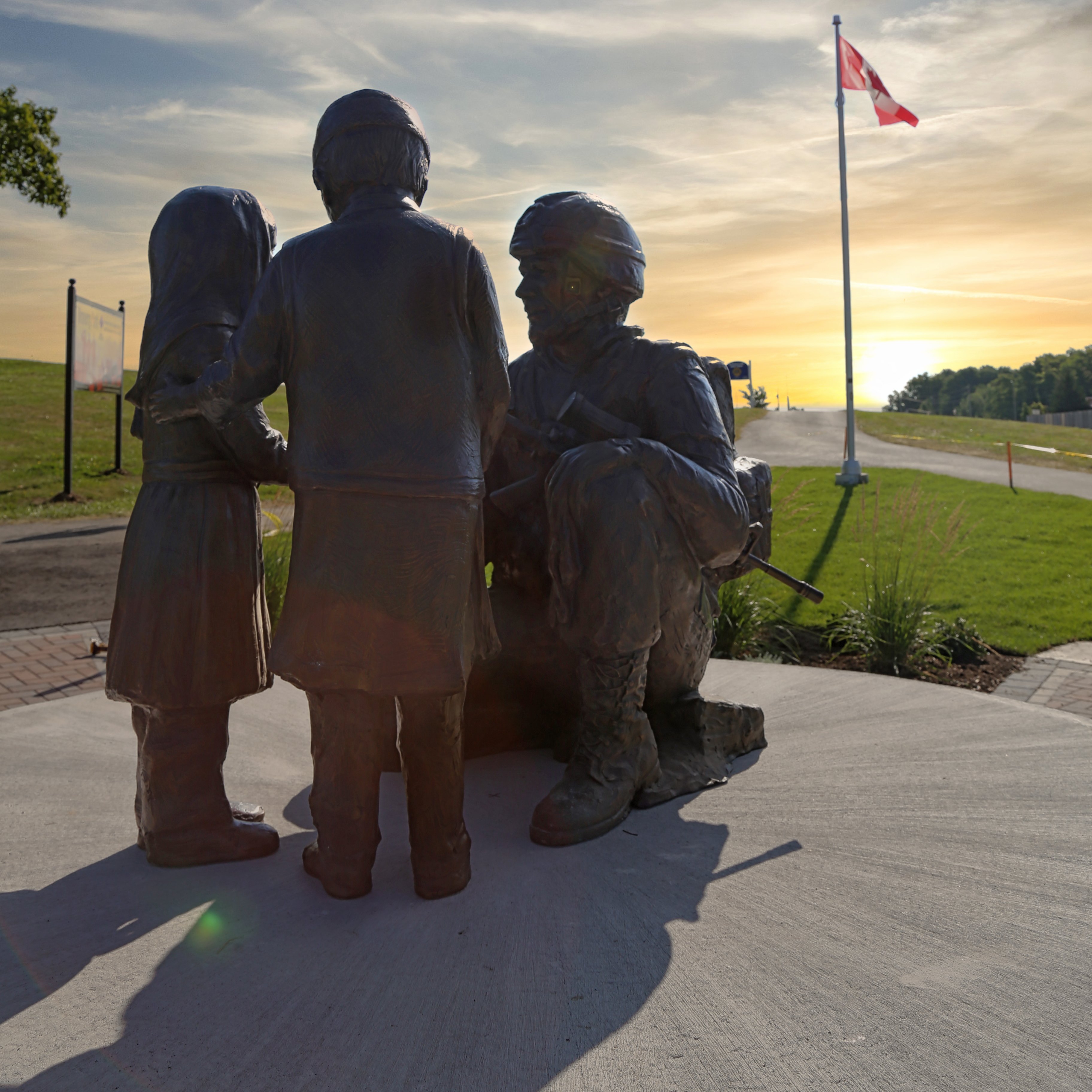 A statue of a soldier holding out his hand to two children, a sunset in the background